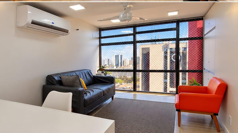 Sala de atendimento com sofá preto, poltrona vermelha e vista para a cidade